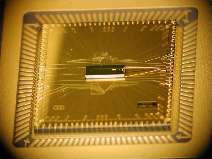 CAPTION A photograph of the completed BGA trap assembly. The trap chip is at the center, sitting atop the larger interposer chip that fans out the wiring. The trap chip surface area is 1mm x 3mm, while the interposer is roughly 1 cm square. CREDIT D. Youngner, Honeywell CAPTION A photograph of the completed BGA trap assembly. The trap chip is at the center, sitting atop the larger interposer chip that fans out the wiring. The trap chip surface area is 1mm x 3mm, while the interposer is roughly 1 cm square. CREDIT D. Youngner, Honeywell